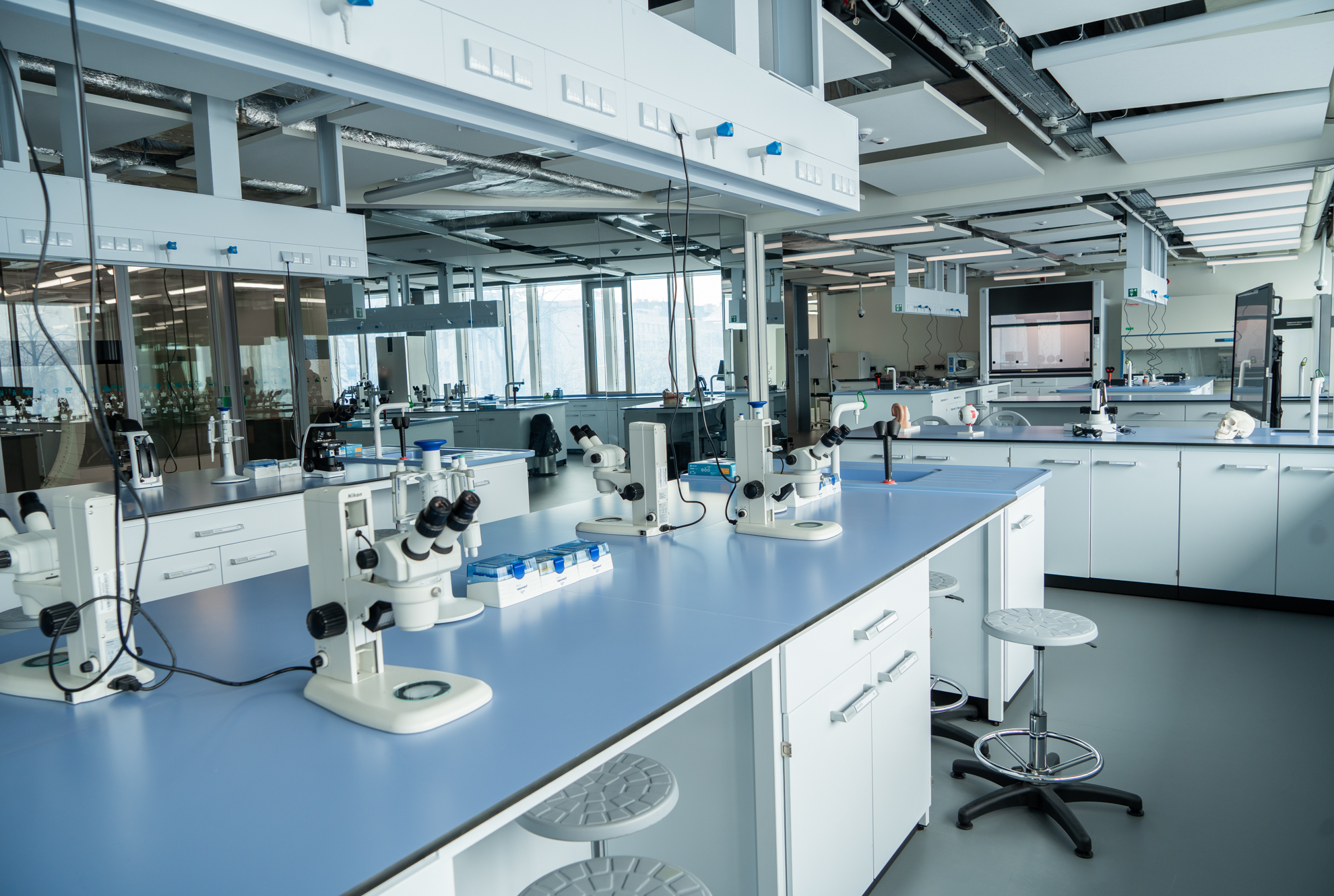 Zdjęcie przedstawia duże pomieszczenie z oknami, stanowiskami pracy, sprzętem (między innymi mikroskopami) i innymi urządzeniami do prowadzenia badań interdyscyplinarnych.